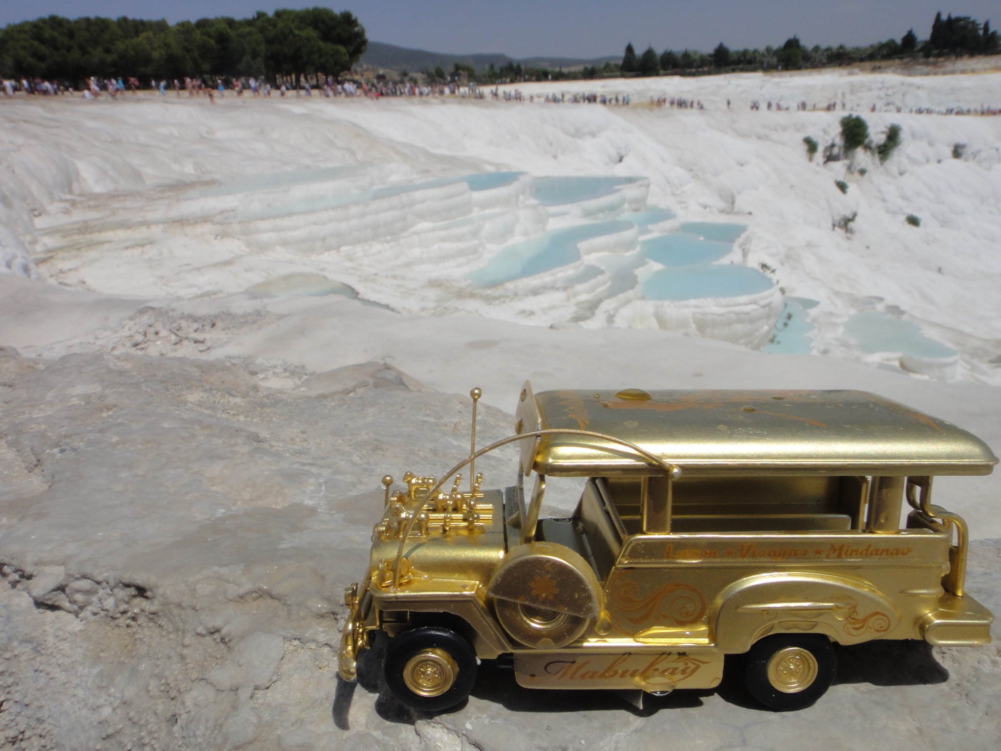 Golden jeepney overlooking the white travertine terraces and blue pools of Pamukkale