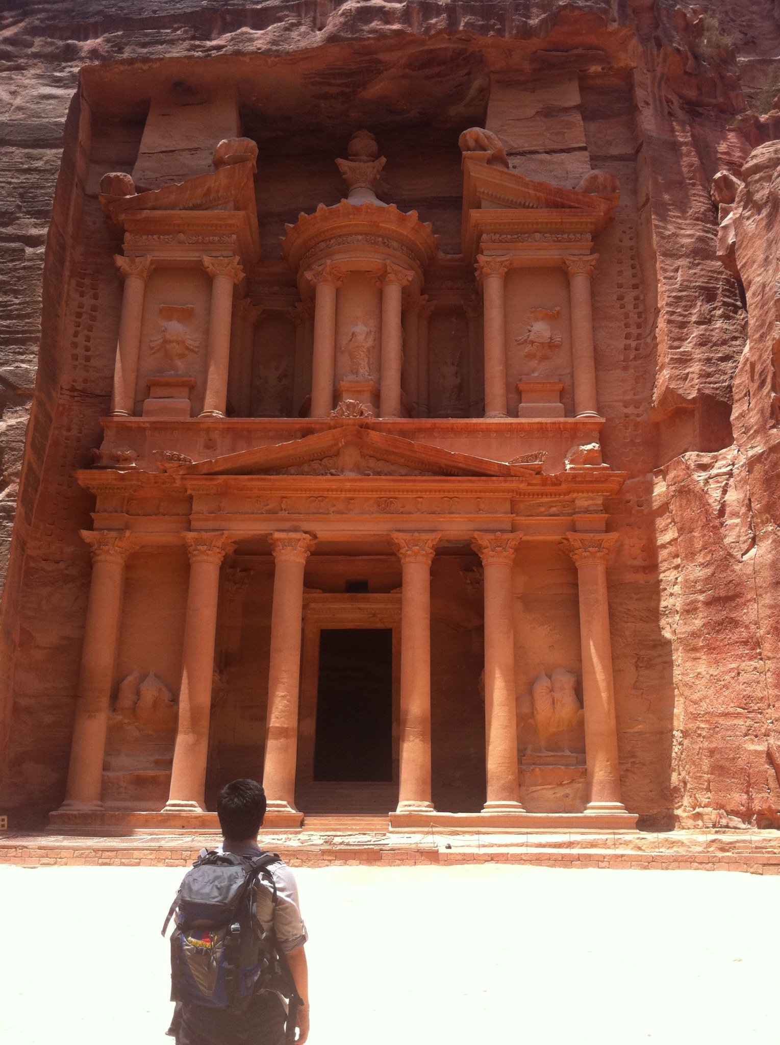 Traveler facing the Treasury carved into the rose-colored cliffs of Petra